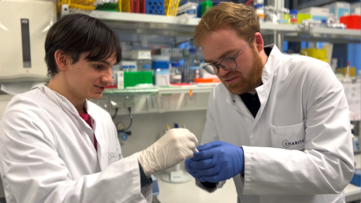 Zwei Forscher stehen nebeneinander in einem Labor und arbeiten gemeinsam ein einem mRNA Forschungsprojekt